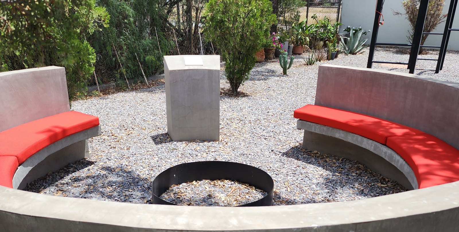 Circular concrete gathering area with benches, fire pit, and memorial plinth